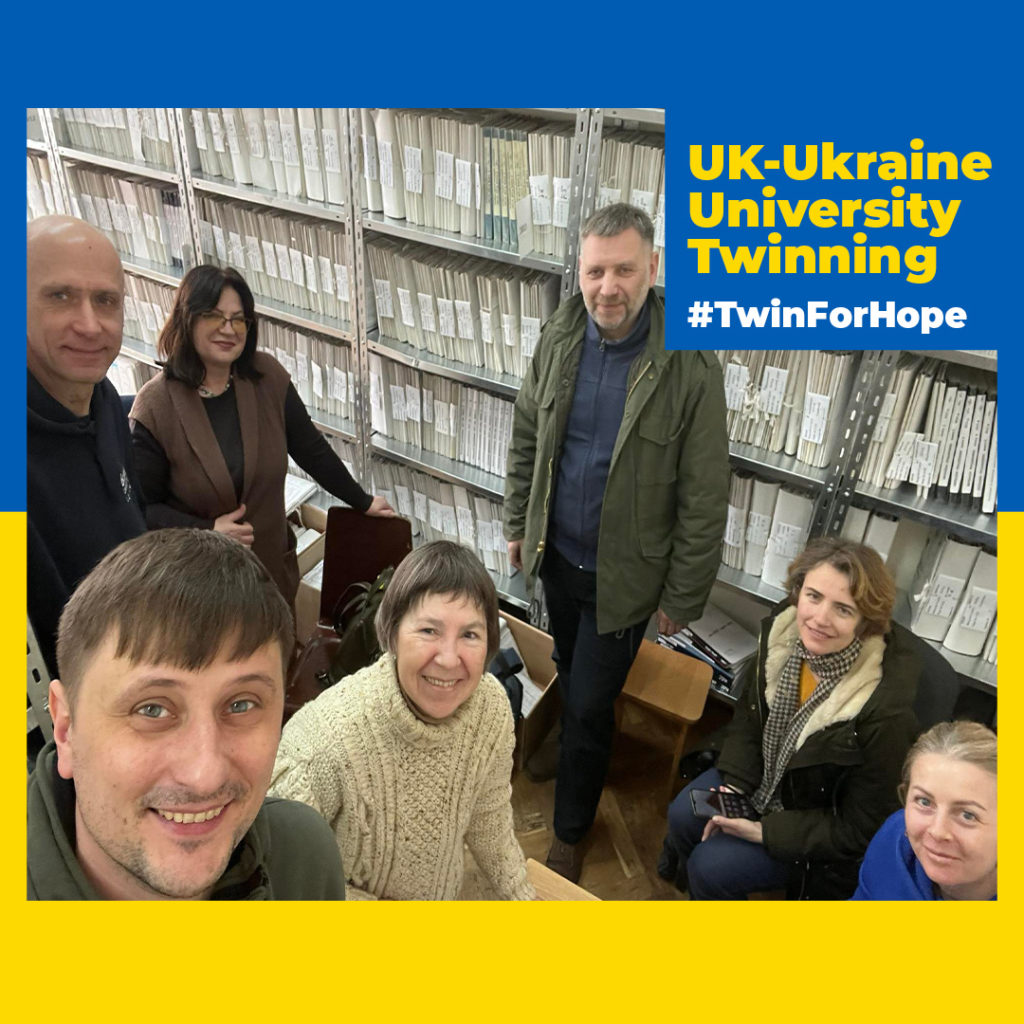 A group of staff from the Lviv National Academy for the Arts gather, smiling, against a backdrop of many archival shelves. The photograph has a border in the blue and yellow of the Ukrainian flag. Text reads: UK-Ukraine University Twinning #TwinForHope