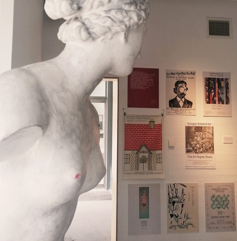 A plaster cast of a classical sculpture overlooks a display of Degree Show posters which date from the 1980s to the 2000s